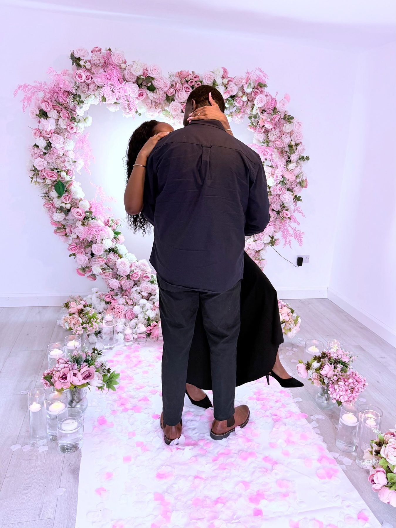 Couple embracing under a pink floral heart arch