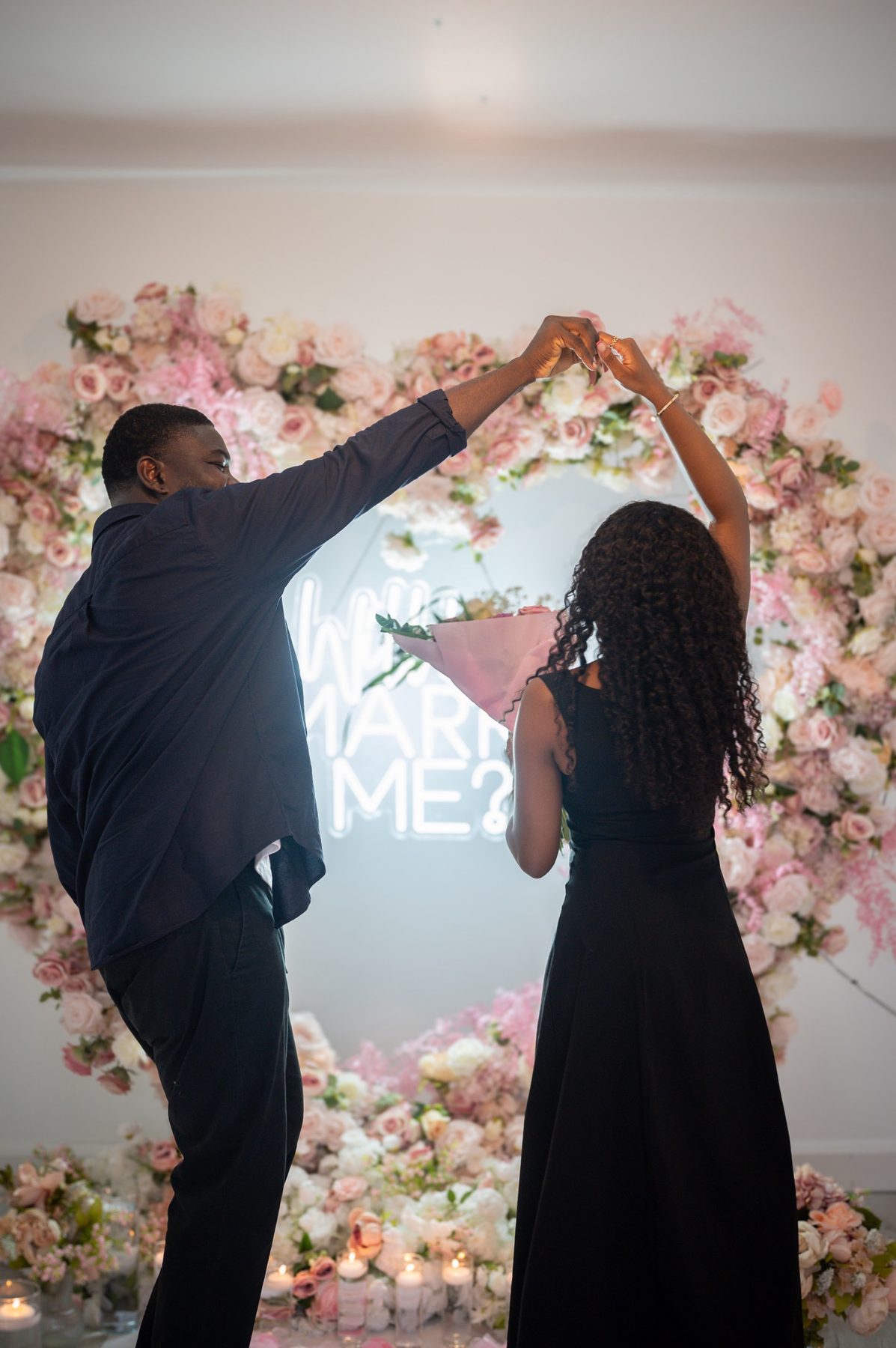 Newly engaged couple dancing in front of a pink floral heart