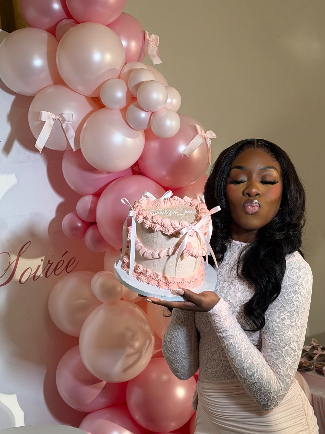 Birthday guest holding a pink cake beside a pink balloon garland