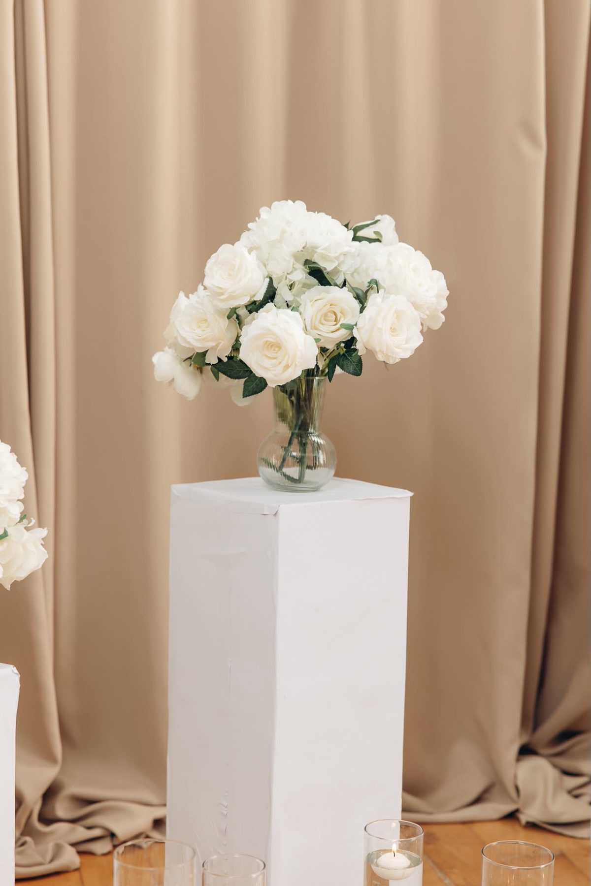 White roses on a white plinth against beige drapes